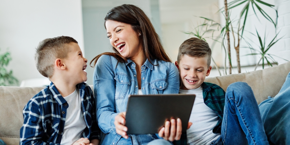 A mother is sitting on the sofa with her two sons, and they are all laughing together.