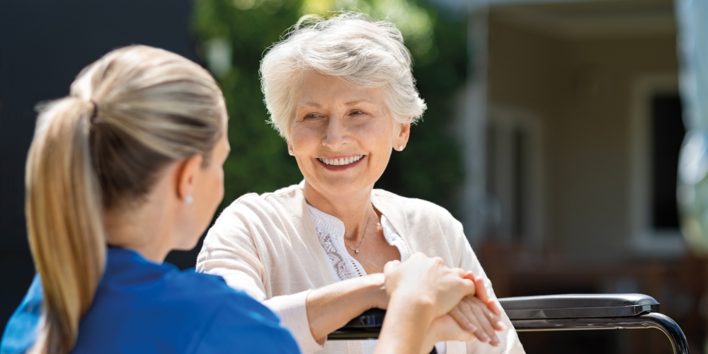 A friendly carer taking care of a happy elderly lady in a wheelchair
