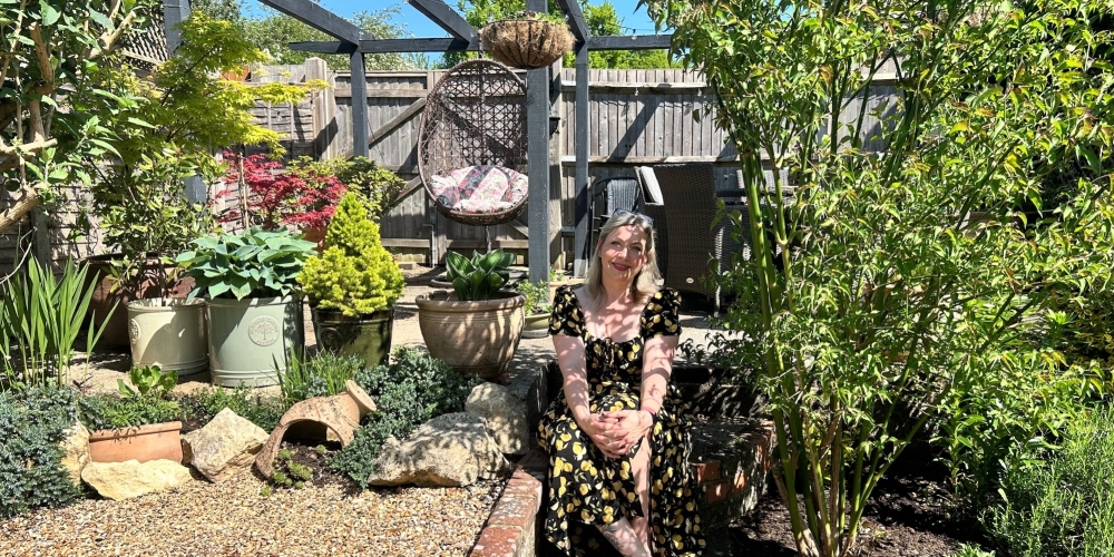 A woman smiling sitting in a garden setting.