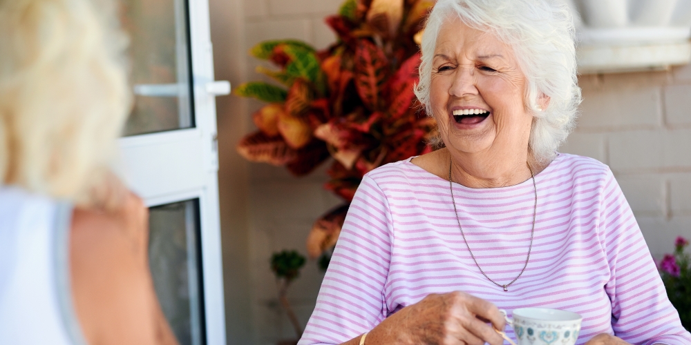An elderly lady sitting in the garden laughing with a friend