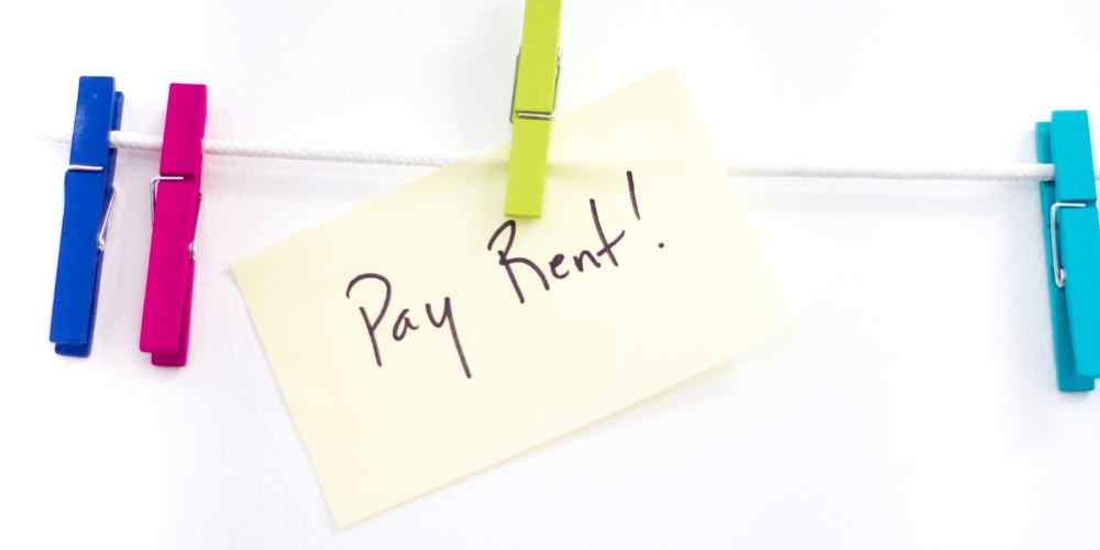 A sticky note reading "Pay Rent!" is pegged on some white string.  