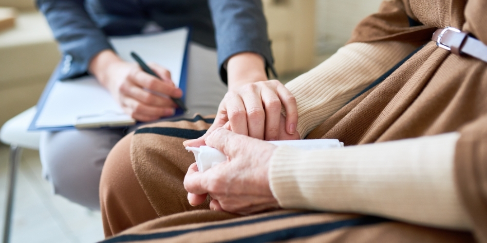 Close-up of a young woman gently holding the hands of an elderly lady.