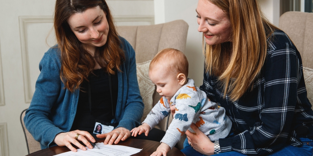 A friendly worker is reviewing paperwork with a single mother and her son on her lap