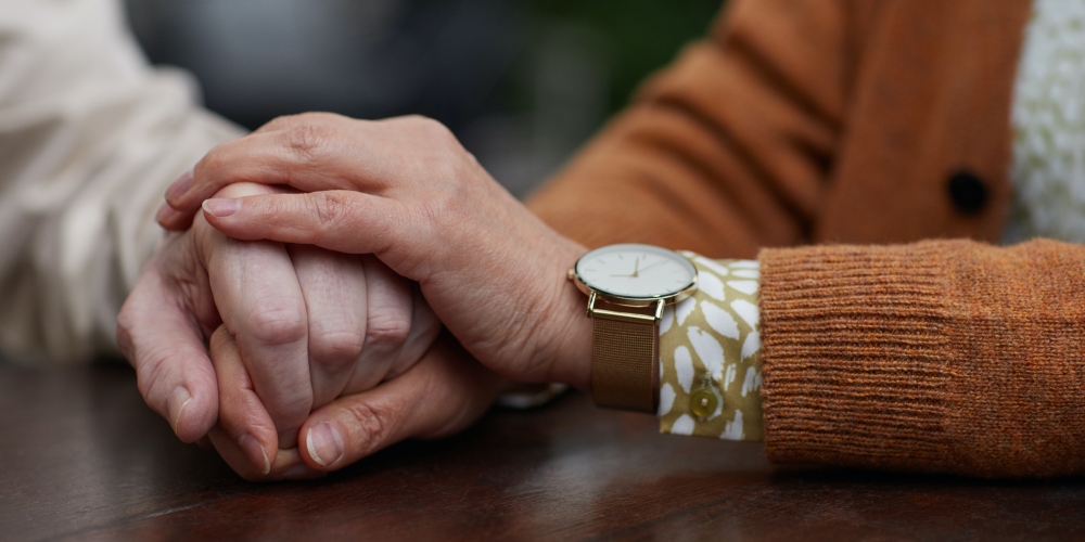 Two elderly friends holding each other’s hands across the table